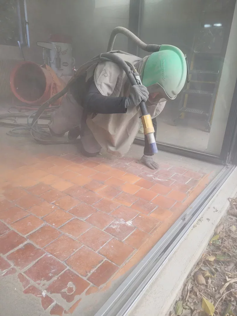 Un homme en casque vert utilise un tuyau pour nettoyer un sol en briques